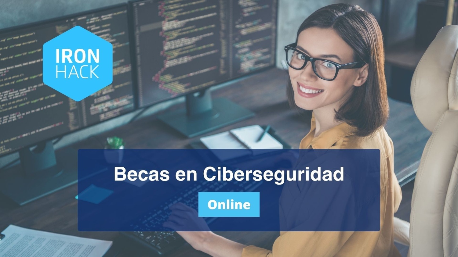 Una mujer sonriente con gafas está sentada en un escritorio monitores de computadora mostrando código. El texto superpuesto dice: Becas en Ciberseguridad, Online. Se ve el logotipo de Ironhack.