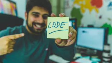 Una persona sonríe y muestra una nota que dice 'code'.