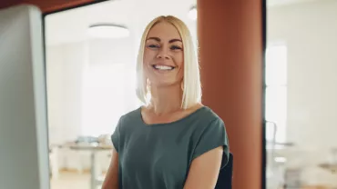 Persona sonriendo frente a una computadora en una oficina iluminada.
