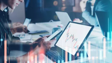 Personas trabajando en laptops con gráficos de datos en pantalla.
