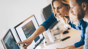 Dos personas revisando código en una computadora.