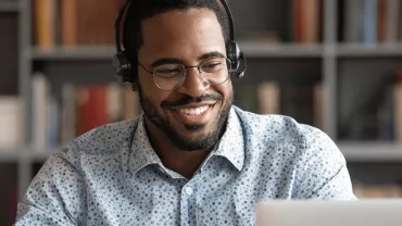 Persona con auriculares sonríe frente a una computadora portátil.