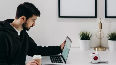 Persona trabajando en una computadora portátil mientras sostiene una taza de café en una oficina moderna.