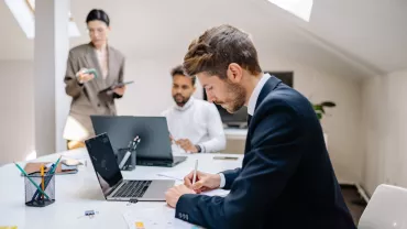 Personas trabajando en una oficina con portátiles y papeles.