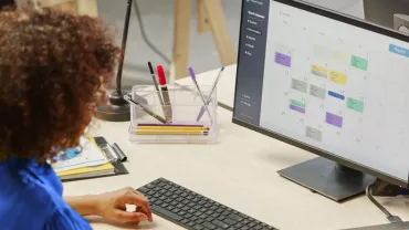 Persona trabajando en un escritorio con una computadora mostrando un calendario.