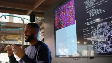 Hombre presentando un proyecto con gráficos y código en una pantalla grande en una oficina 