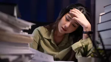 Persona mirando papeles rodeada de pilas de documentos y libros.