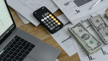 Imagen de una mesa con notas, ordenador, calculadora y billetes
