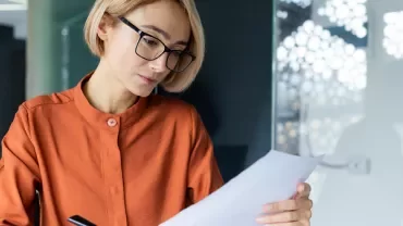 Mujer rubia con gafas leyendo un documento.