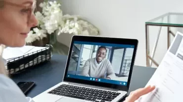 Mujer haciendo una entrevista de trabajo online mirando el CV del candidato que aparece en la pantalla de su ordenador