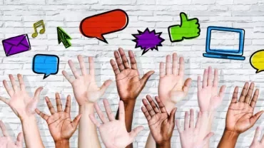 manos de diferentes colores alzadas e iconos de conversación dibujados en una pared blanca