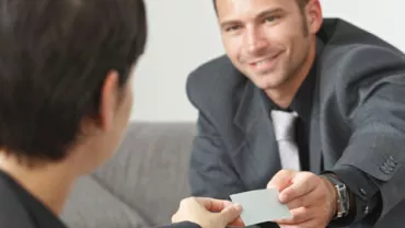 Persona entregando una tarjeta a otra persona en una reunión.