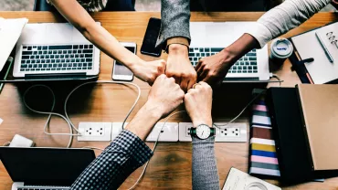 Cinco manos unidas sobre una mesa de oficina.