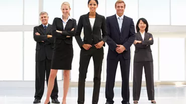 Un grupo de profesionales en traje sonríe en una oficina luminosa.