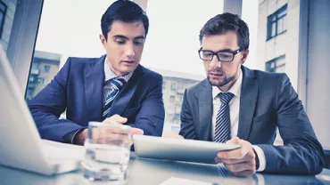Dos personas en trajes revisan un documento en una oficina.