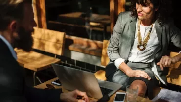 Dos personas conversan en una cafetería al aire libre.