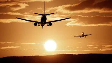 Dos aviones aterrizan al atardecer con el sol en el horizonte.