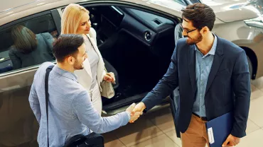 Personas estrechando manos en un concesionario de coches.