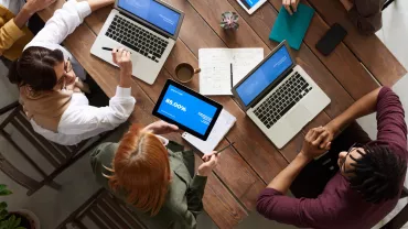 Reunión de grupo alrededor de una mesa con portátiles y tablets.