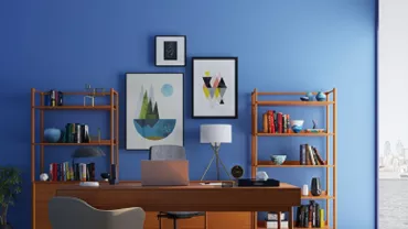 Una oficina con escritorio de madera y estantes llenos de libros, contra una pared azul con arte.