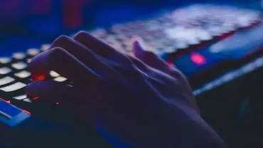 Mano sobre teclado iluminado por luces azules.