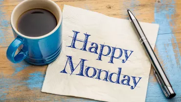 Taza de café y bolígrafo al lado de servilleta que dice 'Happy Monday'.