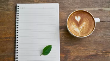 Taza de café con latte arte y cuaderno sobre mesa de madera