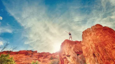 Persona en la cima de una montaña de roca roja bajo un cielo despejado.