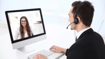 Persona en videollamada con auriculares, trabajando frente a un ordenador.