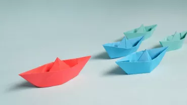 Botes de papel en fila, uno rojo y otros azules.