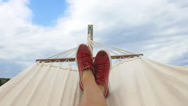 Relajación en una hamaca con zapatos rojos bajo el cielo azul.