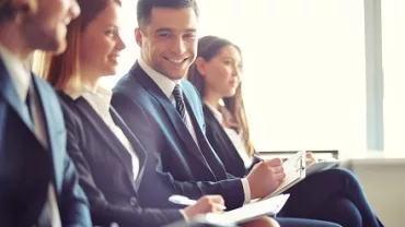 Grupo de personas en trajes formales sonriendo en una reunión.