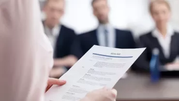 Persona sosteniendo un currículum durante una entrevista de trabajo frente a tres personas.