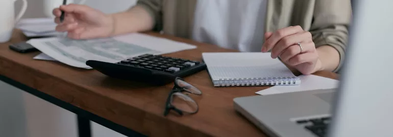 Persona usando calculadora y tomando notas en un escritorio.