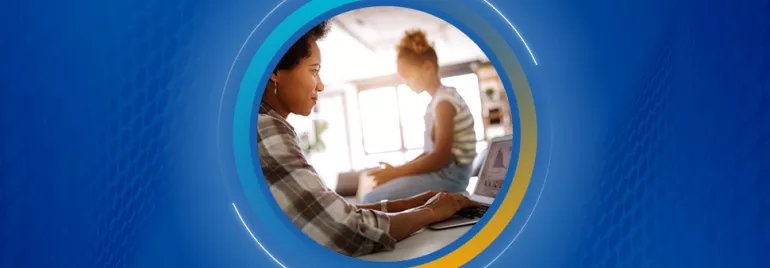Persona trabajando en una computadora mientras otra persona está sentada cerca.