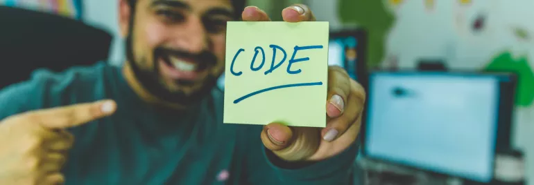 Una persona sonríe y muestra una nota que dice 'code'.