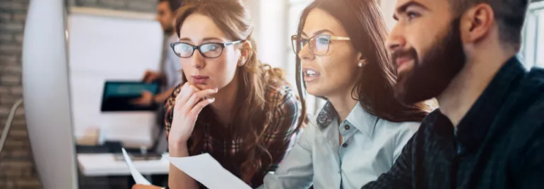 Tres personas discuten frente a un monitor en una oficina moderna.