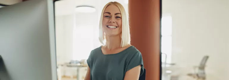 Persona sonriendo frente a una computadora en una oficina iluminada.
