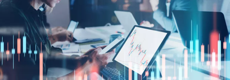 Personas trabajando en laptops con gráficos de datos en pantalla.