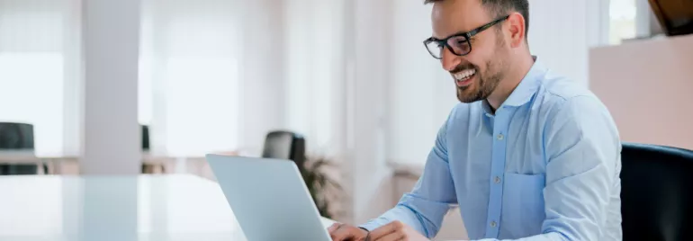 Persona sonriendo mientras usa una computadora portátil en una oficina.