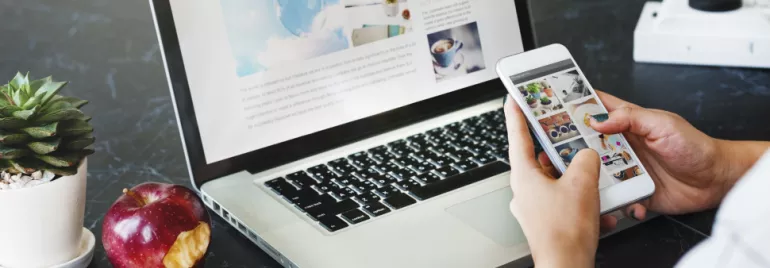 Persona usando un teléfono y una laptop en una mesa con una manzana y suculenta.