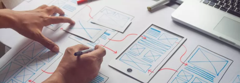 Persona diseñando una aplicación móvil con bocetos en papel.