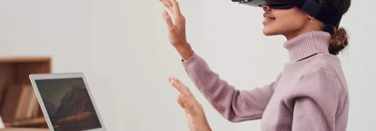 Persona usando una realidad virtual mientras está sentada frente a una computadora portátil.