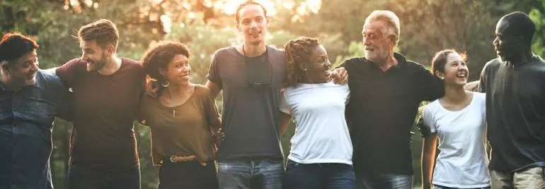 Grupo diverso de personas al aire libre, sonriendo y abrazándose al atardecer.