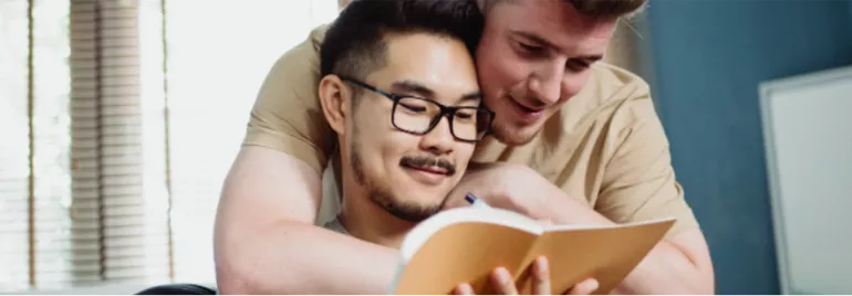 Dos personas leyendo un libro juntas en una habitación luminosa.