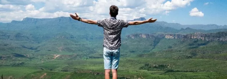 Persona en la cima de una montaña con los brazos abiertos hacia el paisaje.