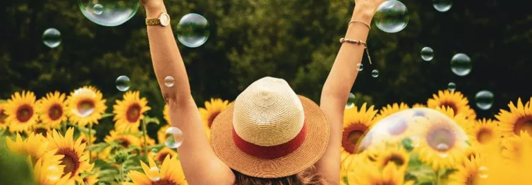 Persona entre girasoles, brazos alzados y burbujas alrededor.