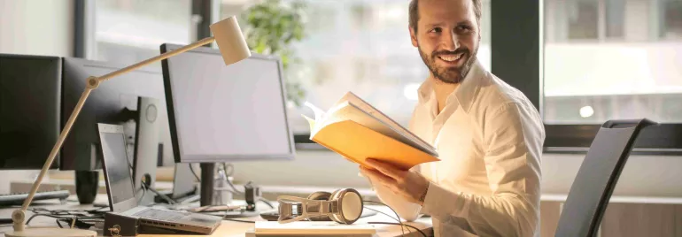 Persona en una oficina sosteniendo un libro, rodeada de computadoras.