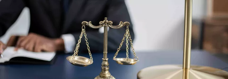 Escala de justicia en un escritorio con lámpara dorada y figura trabajando de fondo.