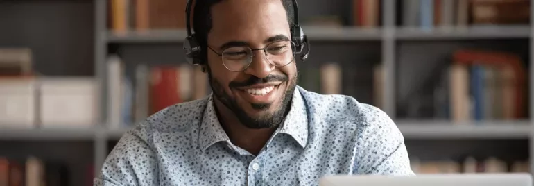Persona con auriculares sonríe frente a una computadora portátil.